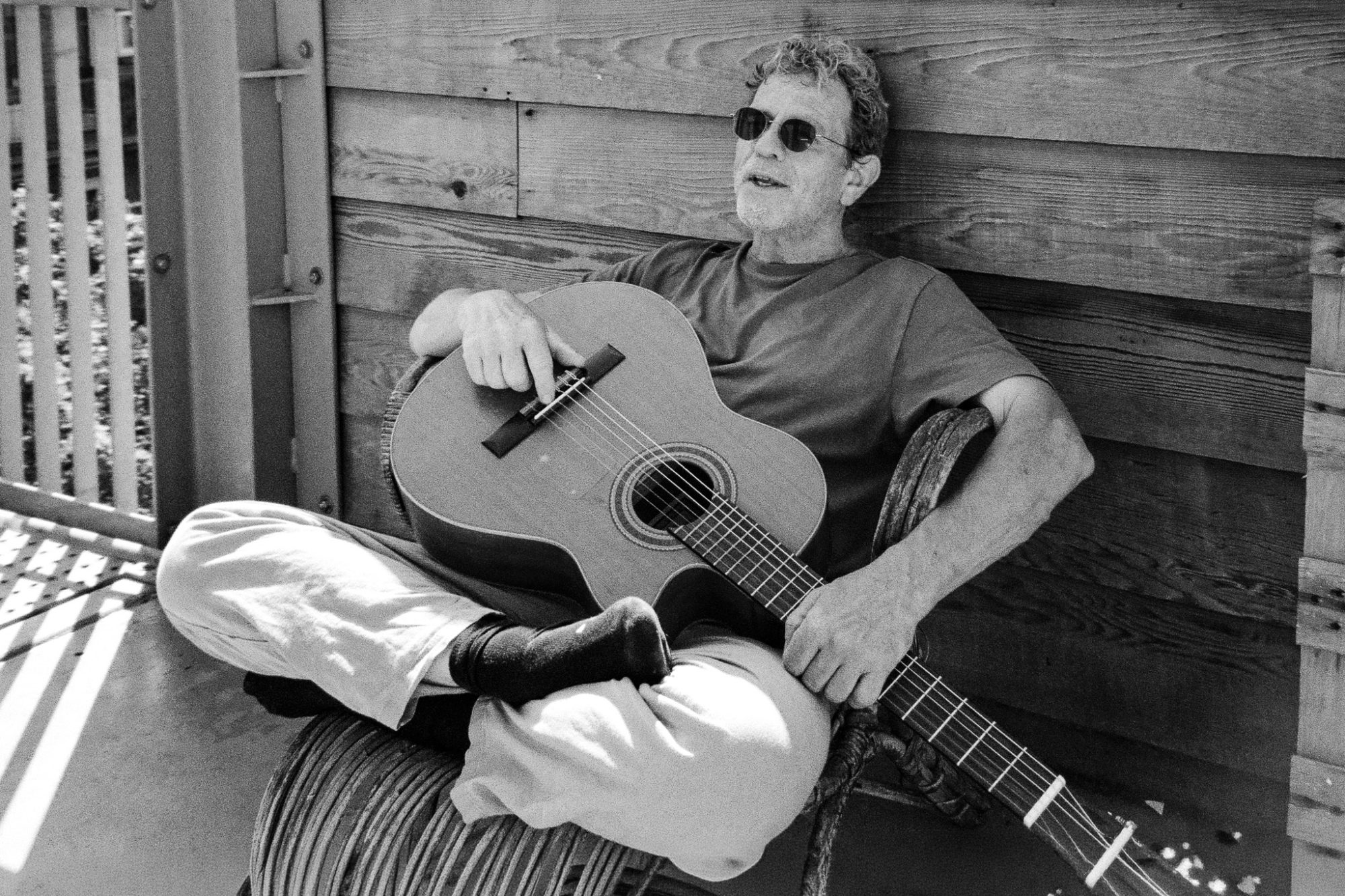 A man with a guitar, against a wooden wall