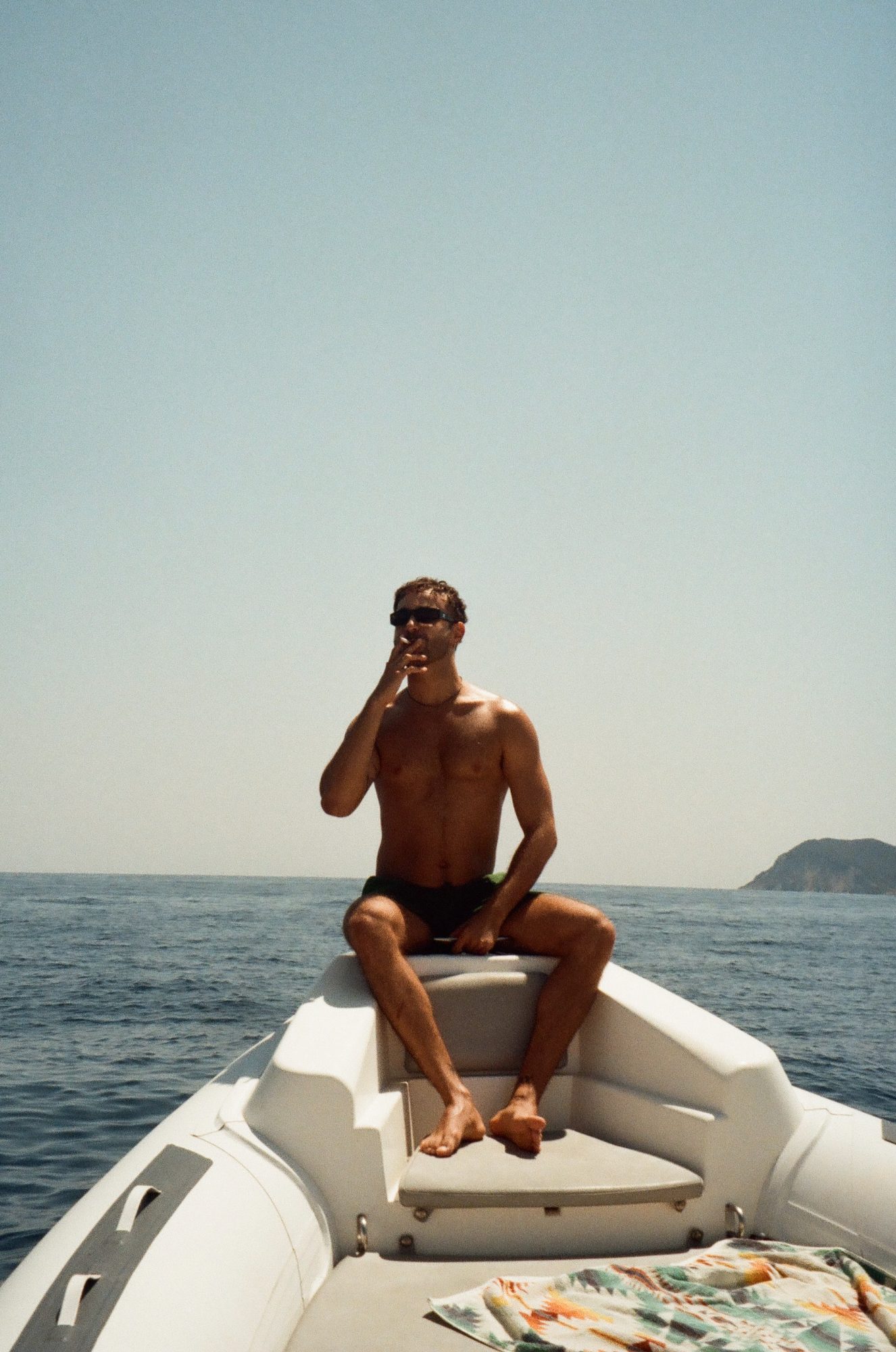 A man smoking on the bow of a boat, an island on the horizon