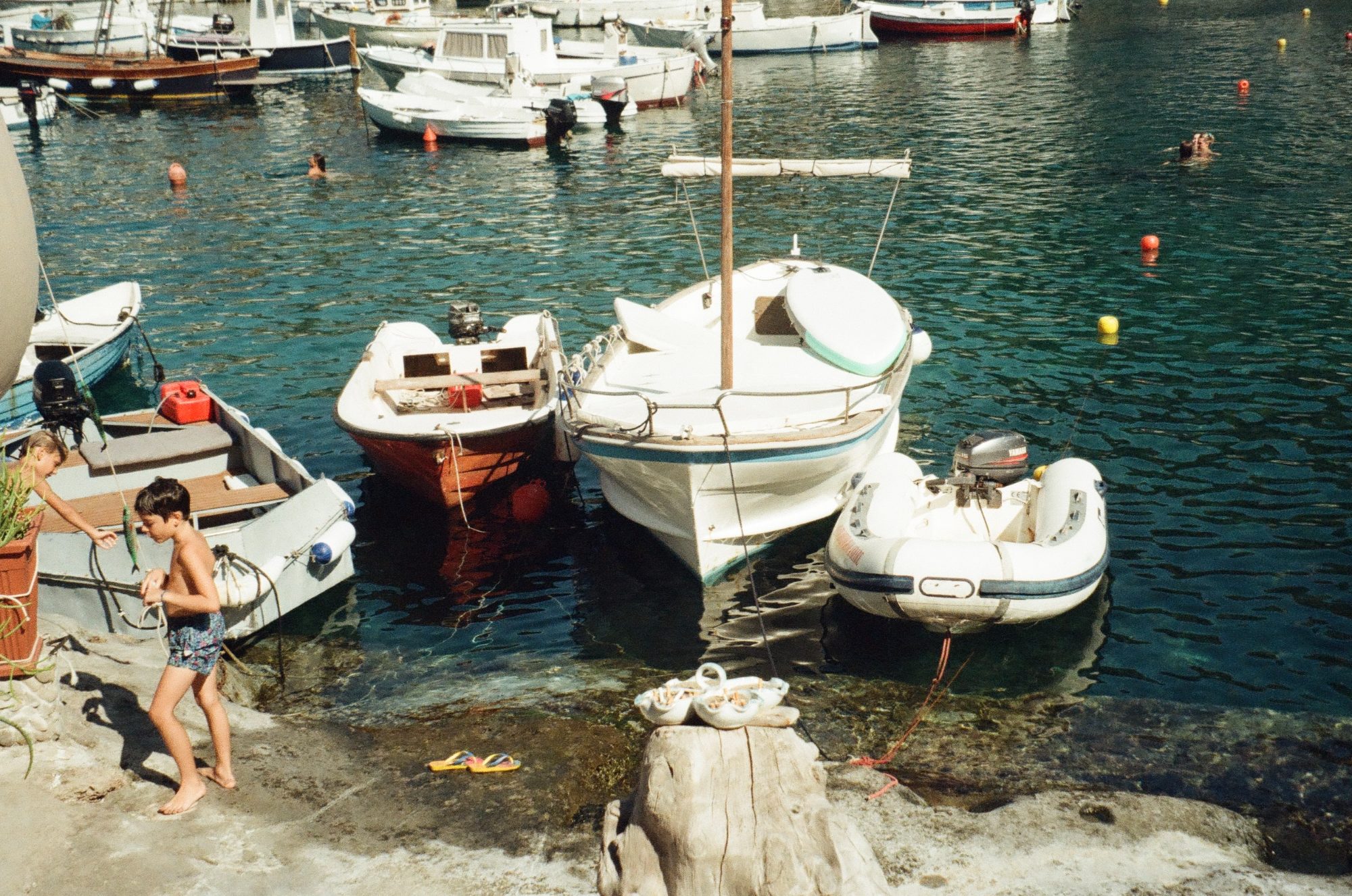 A boy carrying a fish along the rocks, moored boats behind