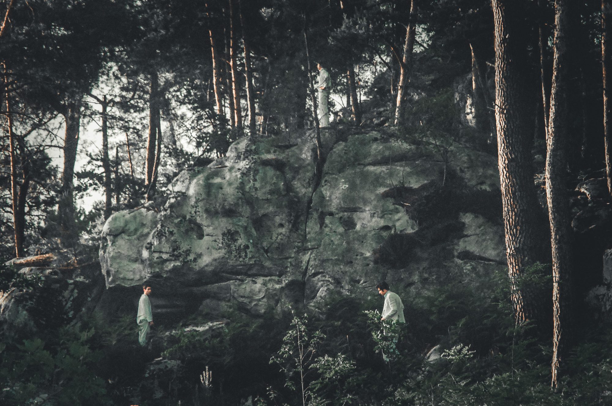 Three figures in white on the rocks, at three heights of the forest